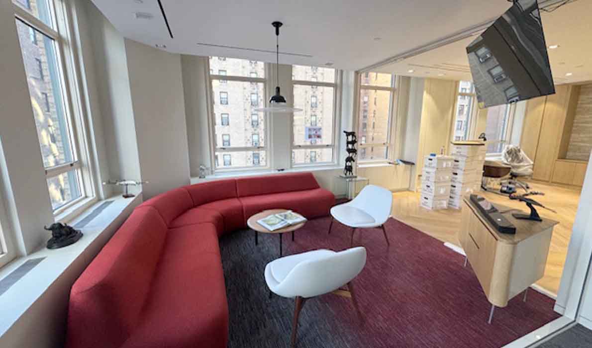 Modern lounge area at 370 7th Avenue renovated by Universal Contracting and Management, featuring a red curved sofa, accent chairs, and large windows with city views.